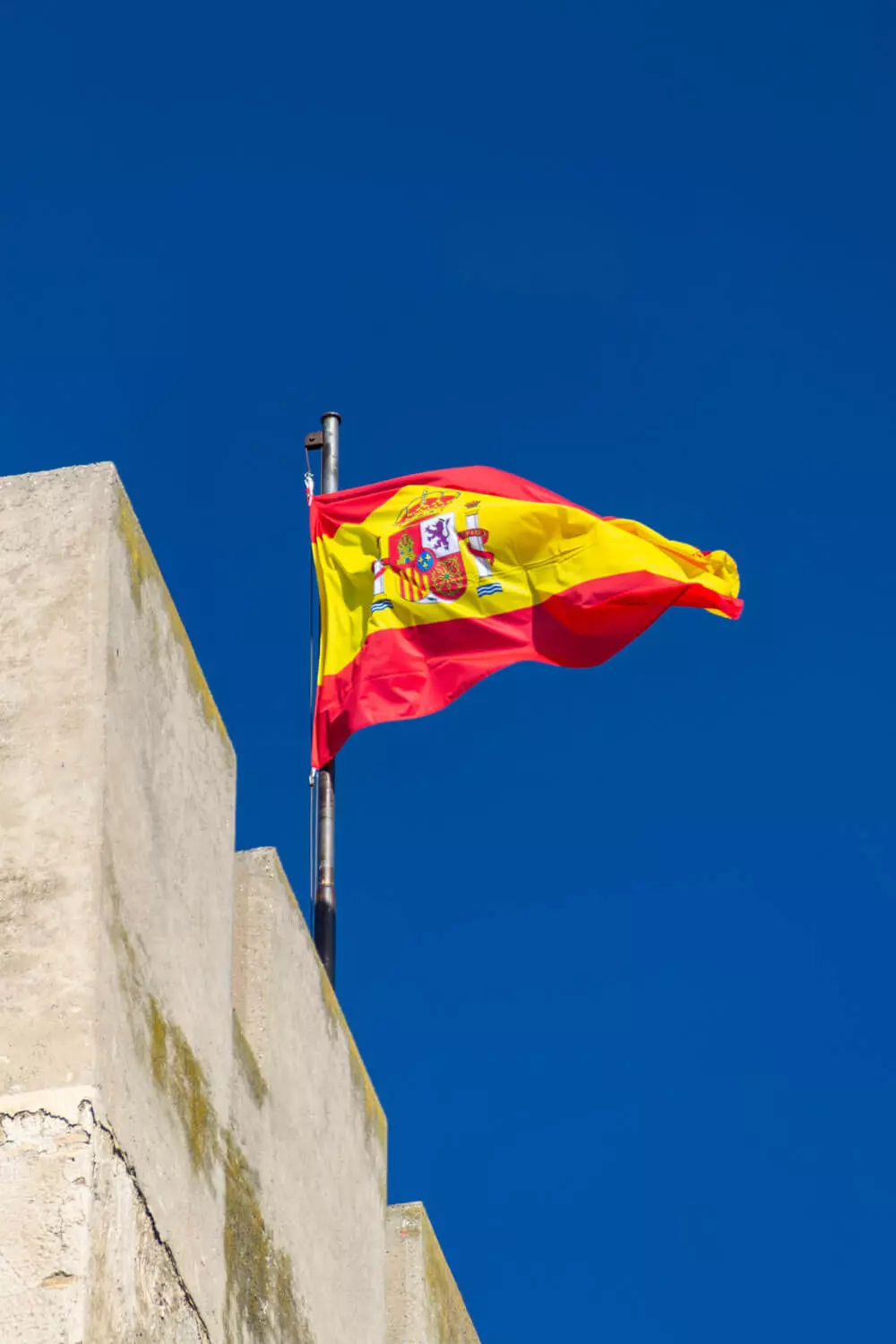 Die gehisste Flagge Spaniens vor blauem Himmel.