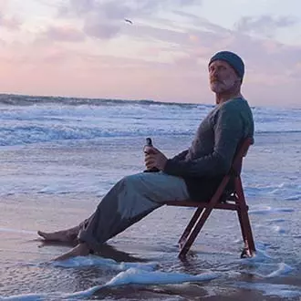 [Translate to English:] Mann sitzt auf einem Hocker am Strand