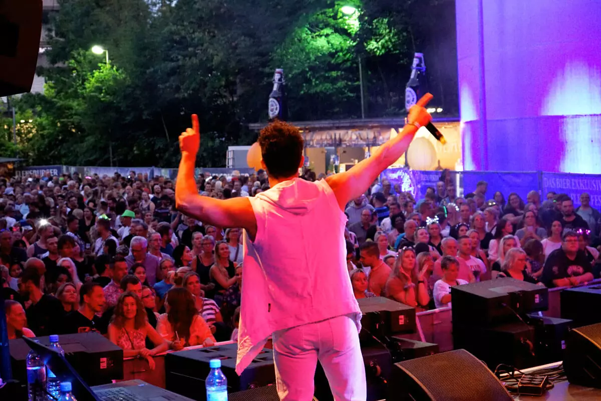Sänger beim FLENS Festival von hinten mit Blick auf das Publikum und das Festivalgelände im violetten Licht.