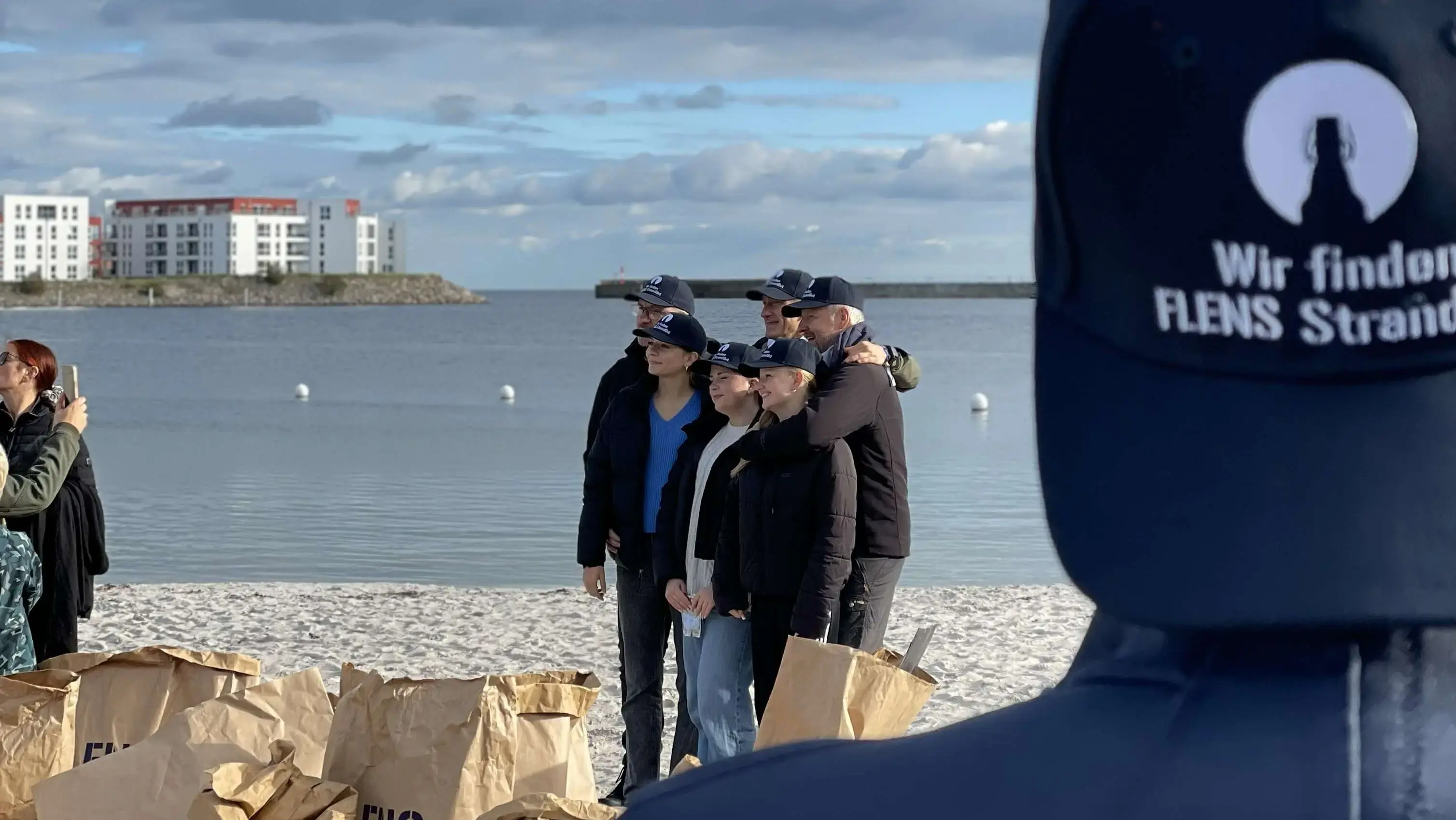 Gruppenfoto einer kleinen Gruppe von Freiwilligen bei einer FLENS StrandGut Aktion, im Vordergrund eine blaue Cap, auf der die Aktion beworben wird.