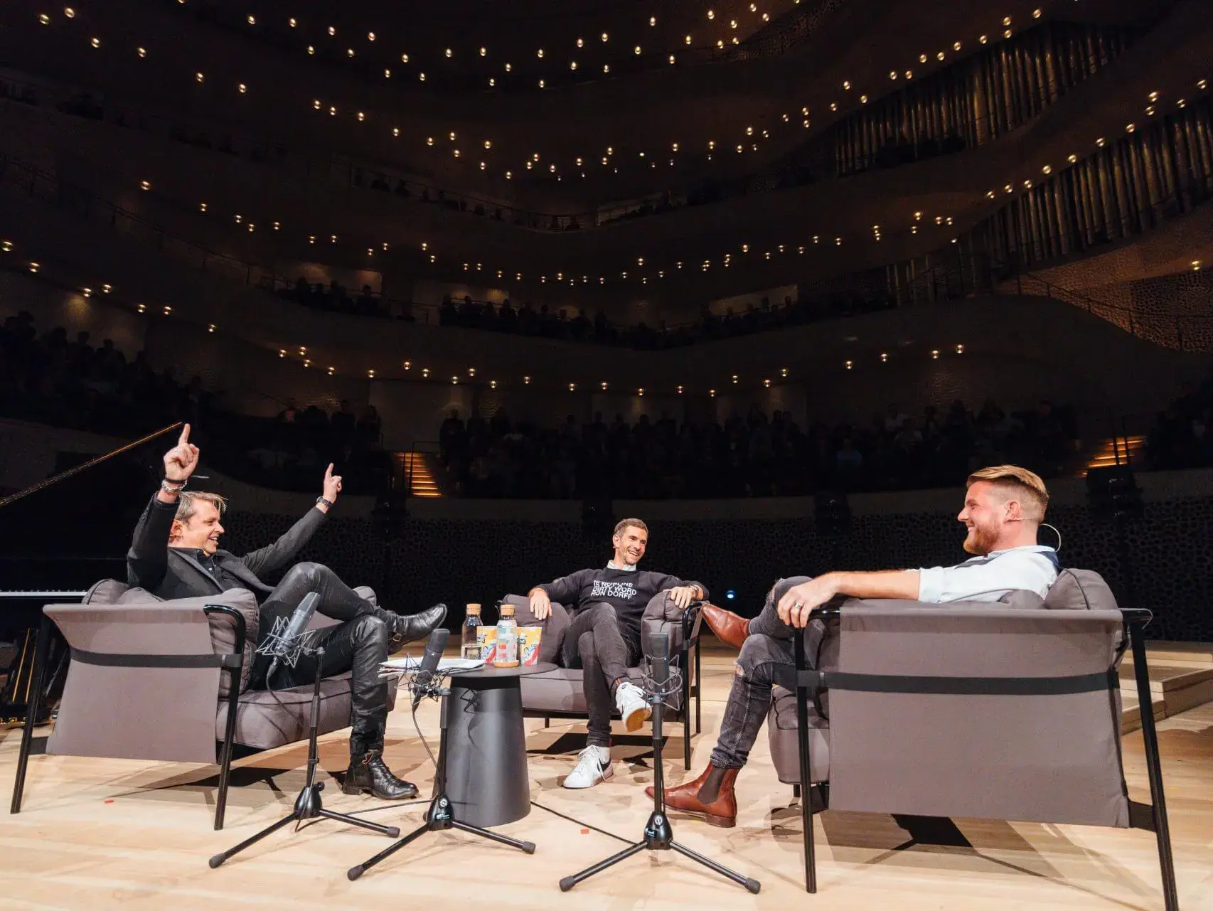 Lebhafte Diskussion der Hosts von FUSSBALL MML in einem modernen Konzertsaal mit Publikum.