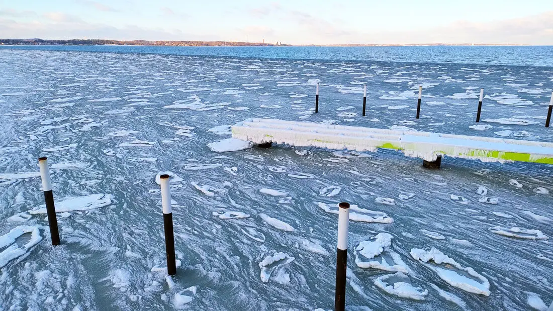 Zugefrorene Ostsee mit vereistem Steg und Pfählen, treibende Eisschollen im Winter.