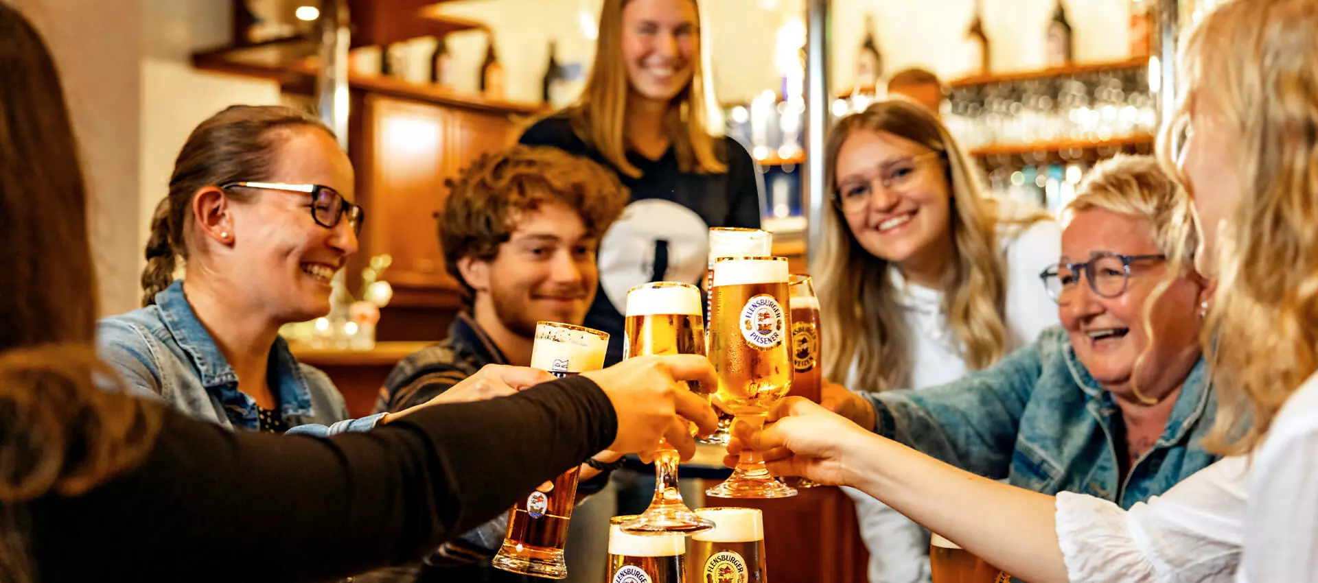 Freudige Gäste im Salon der Flensburger Brauerei, die mit Biergläsern anstoßen.