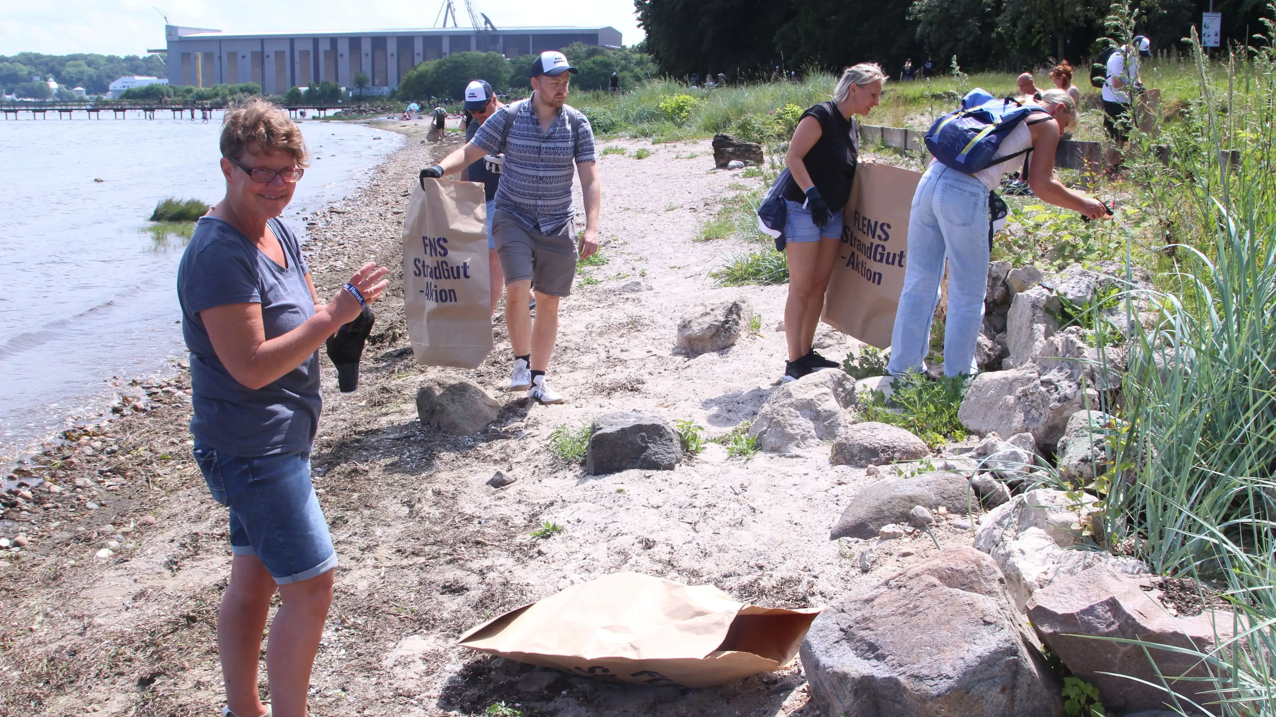 Frauen und Männer sammeln Müll am Flussufer bei einer FLENS Strandreinigungsaktion.
