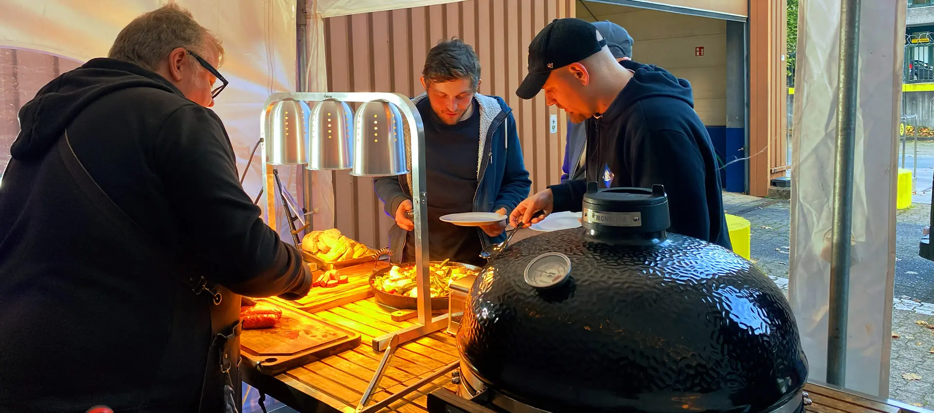 Die Gewinner bedienen sich an der Vorspeise bei der Grillweltmeisterparty von FLENS, rechts der große Kugelgrill von Grillweltmeister Marco Greulich, links im Bild.