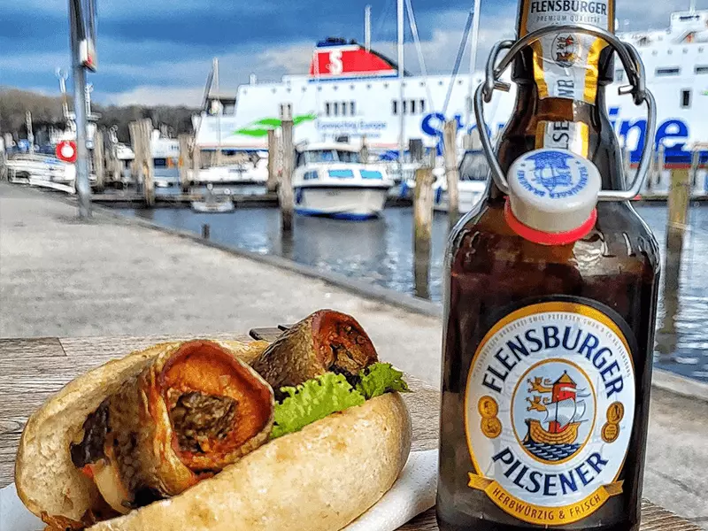 Flensburger Pilsener mit einem Fischbrötchen am Hafen.