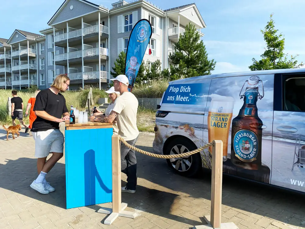 Flensburger Strand-Lager Bierpromo mit Van und Tresen an Strandpromenade in Heiligenhafen vor Ferienwohnungen.