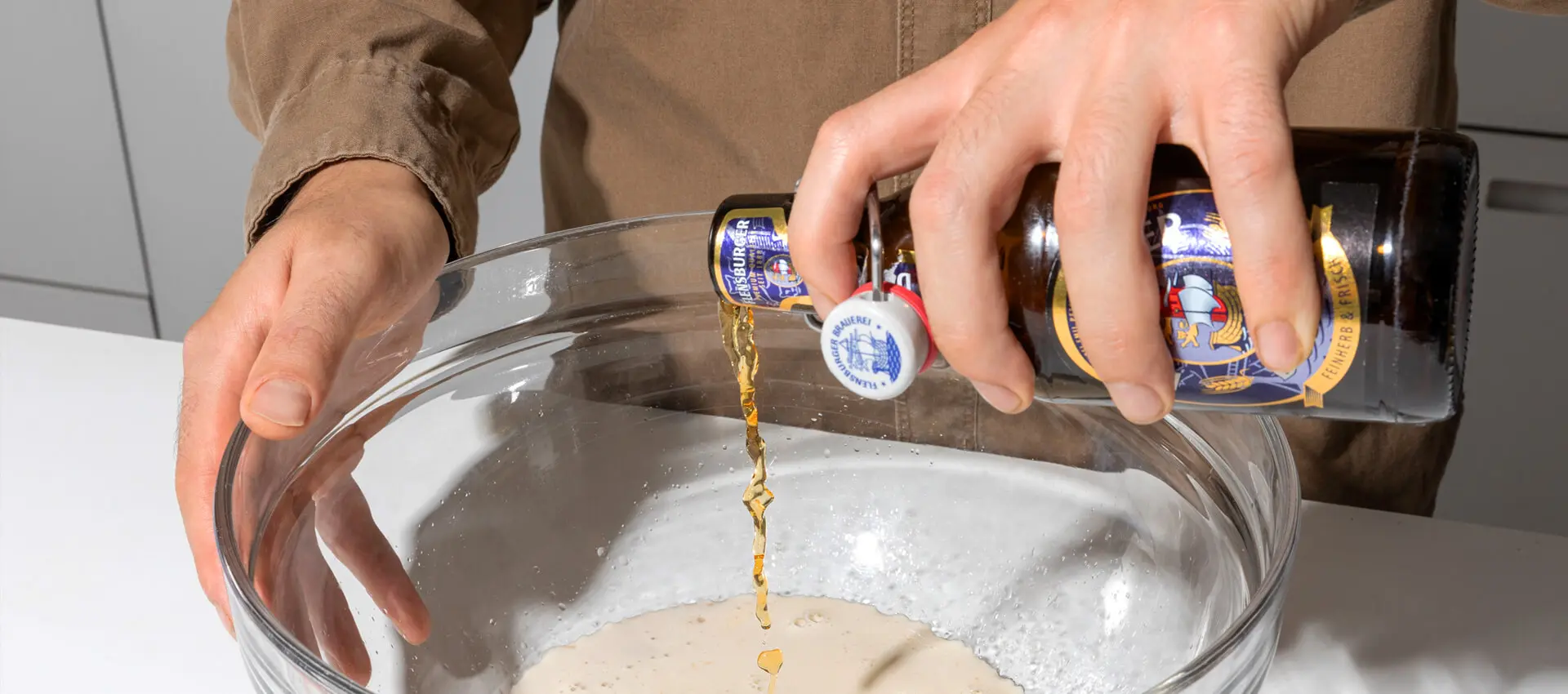 Hände gießen Flensburger Dunkel aus Bügelflasche in eine große Glasschüssel mit Mehl.