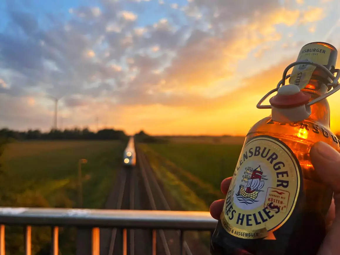 Eine Flasche Flensburger Edles Helles, durch die die Sonne scheint, auf einer Bahnübergangsbrücke.
