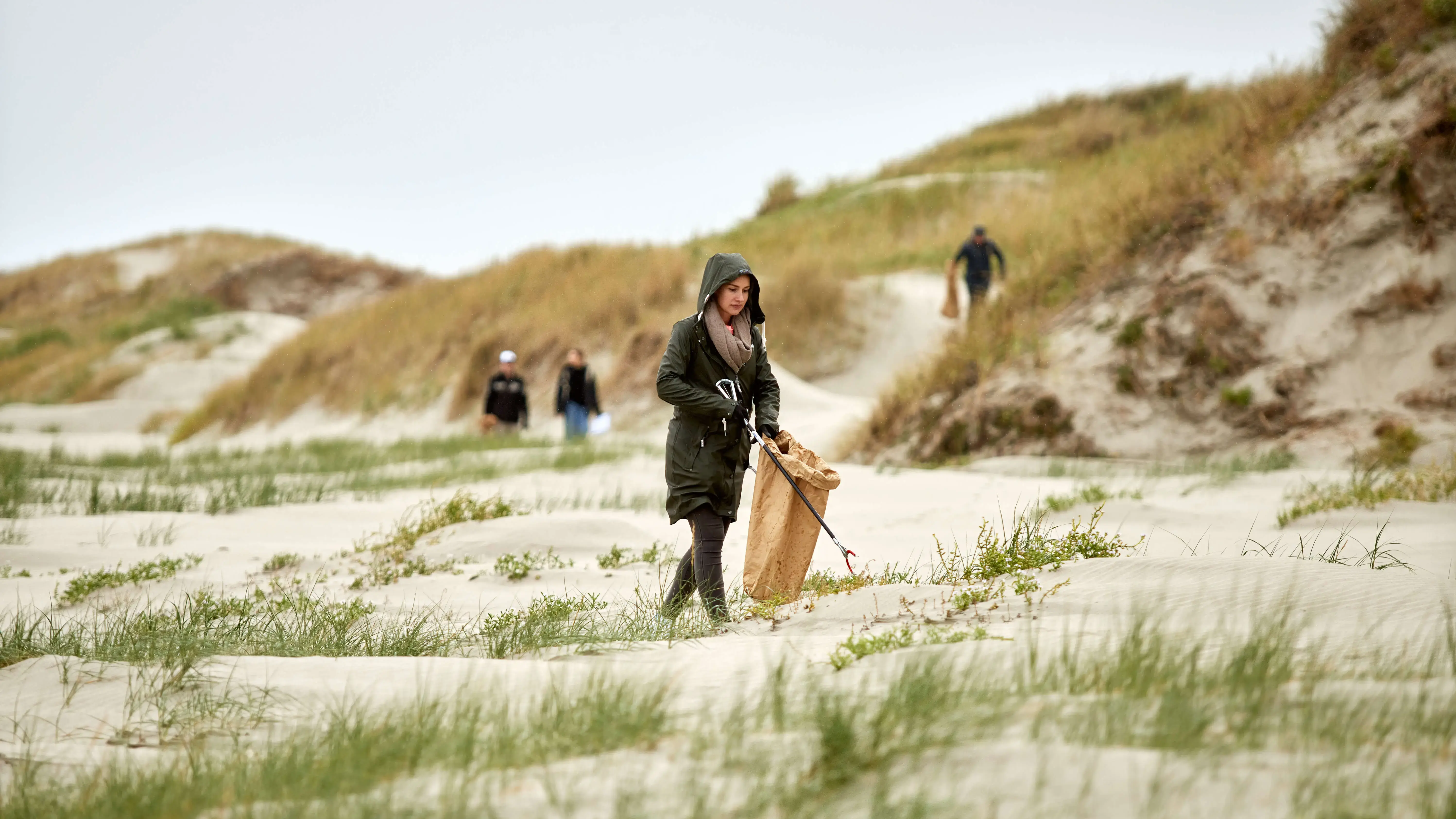Frau sammelt Müll in den Dünen am Strand bei einer FLENS StrandGut Aktion.