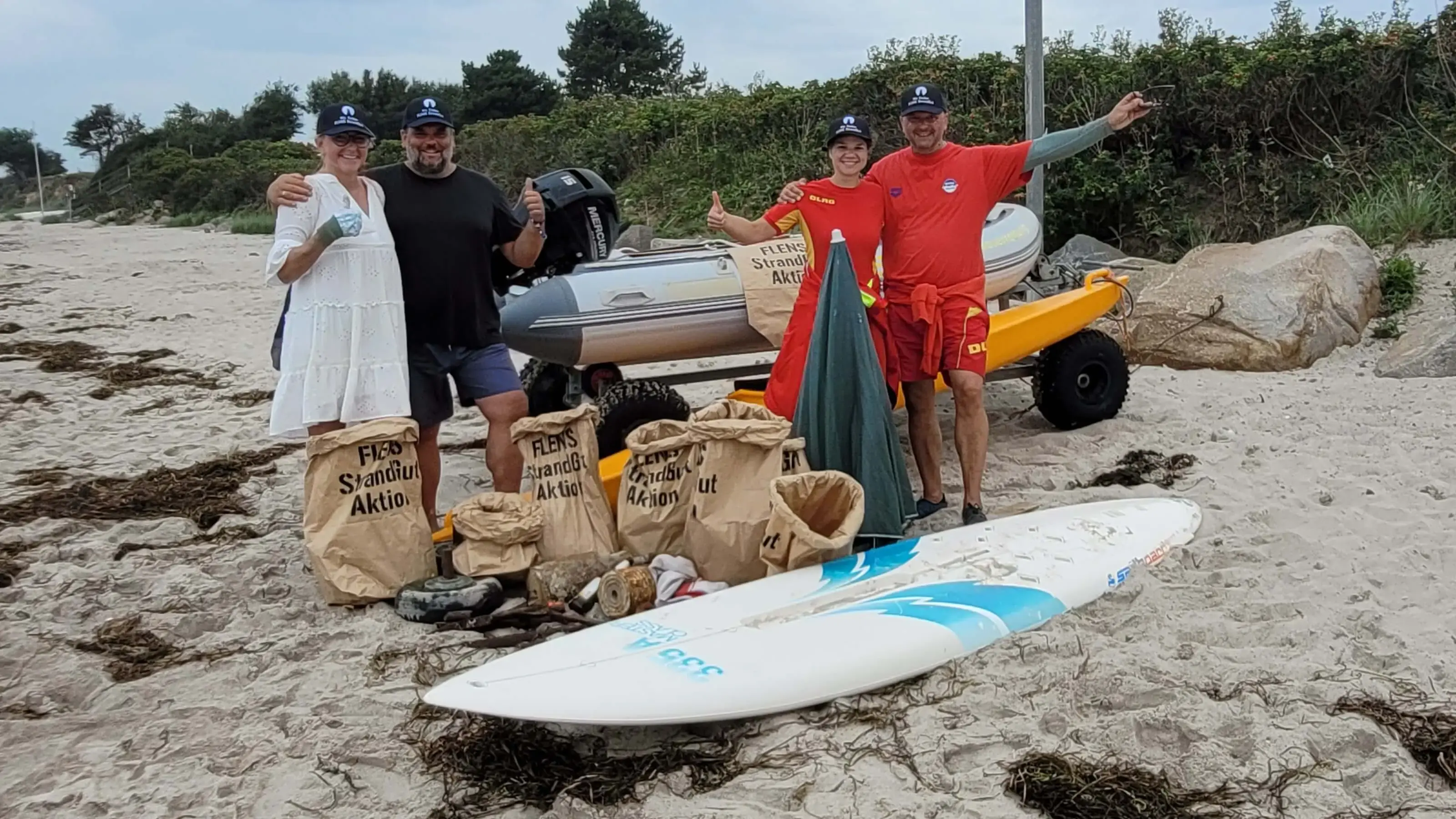 Freiwillige sammeln Müll am Strand mit Surfbrett und Schlauchboot im Rahmen einer FLENS StrandGut Aktion.