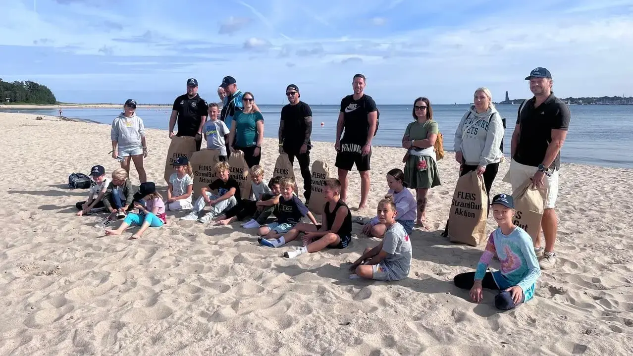 Gruppe von Erwachsenen und Kindern an einem sonnigen Strand bei einer FLENS StrandGut Aktion.