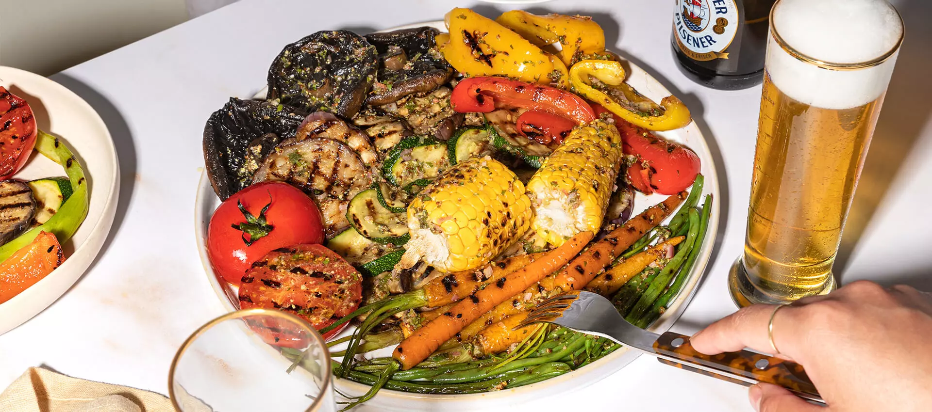 Buntes Grillgemüse mit Bierdressing, auf einem Teller, neben einem FLENS im Glas.