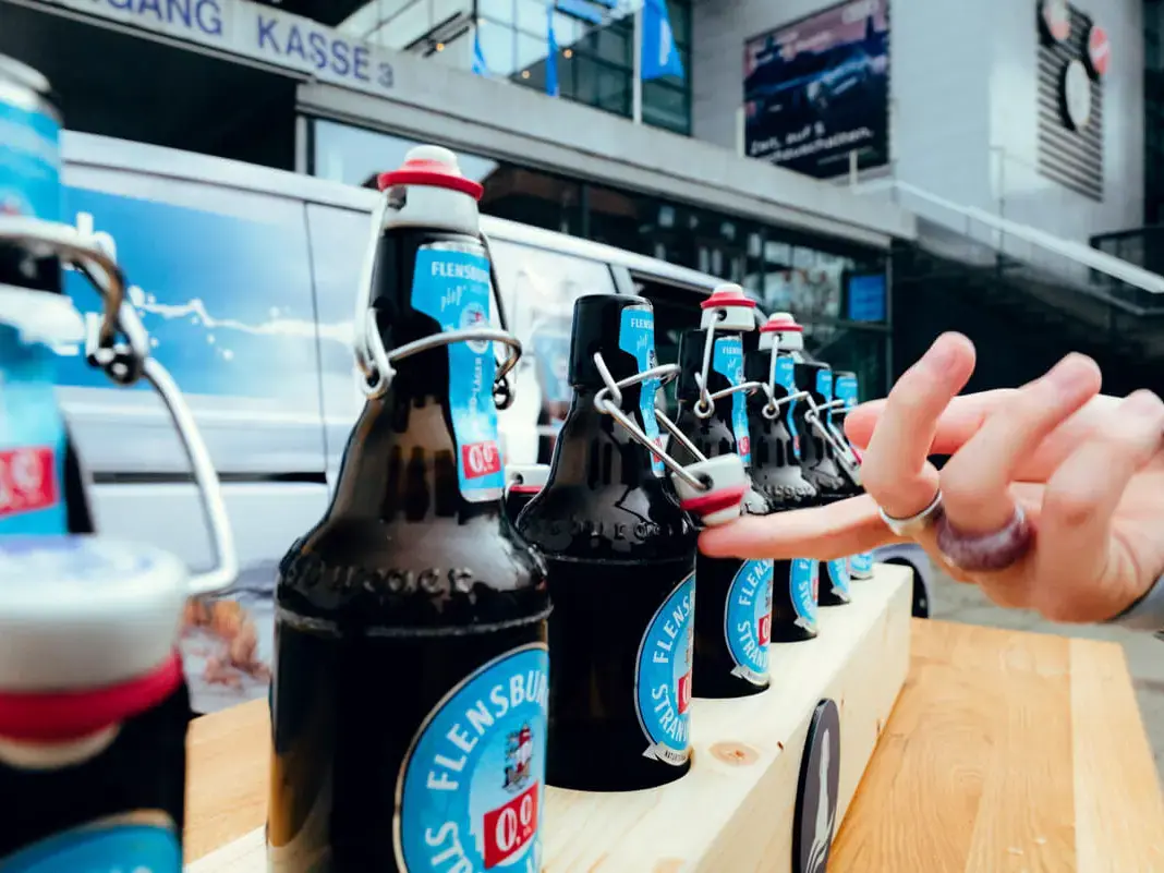 Flensburger Bügelflaschen auf Holzbrett, eine Hand am Bügelverschluss beim Prömpelspiel im Freien.