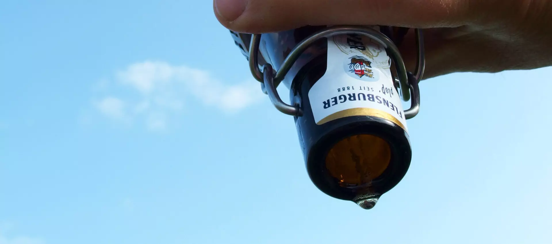 Offene Bierflasche, die von einer Hand über Kopf gehalten wird.