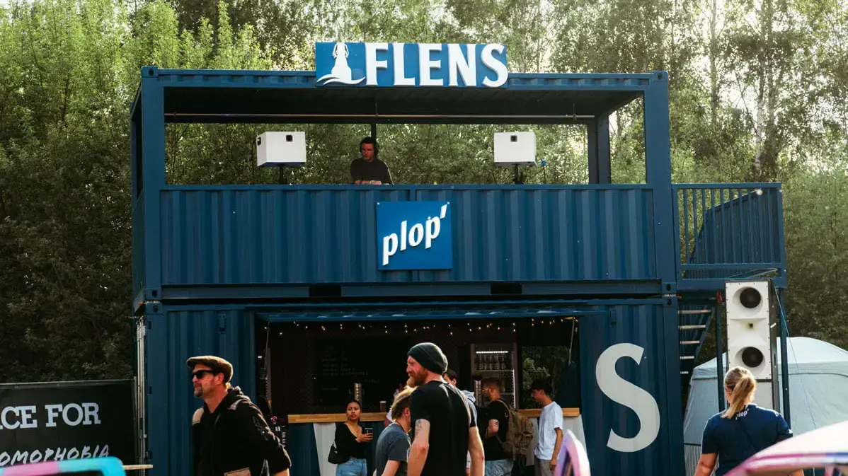 Blauer, zweistöckiger Container-Festivalstand 'FLENS' mit DJ-Dach, Bar und Besuchenden beim Butcher-Jam-Festival 2026.