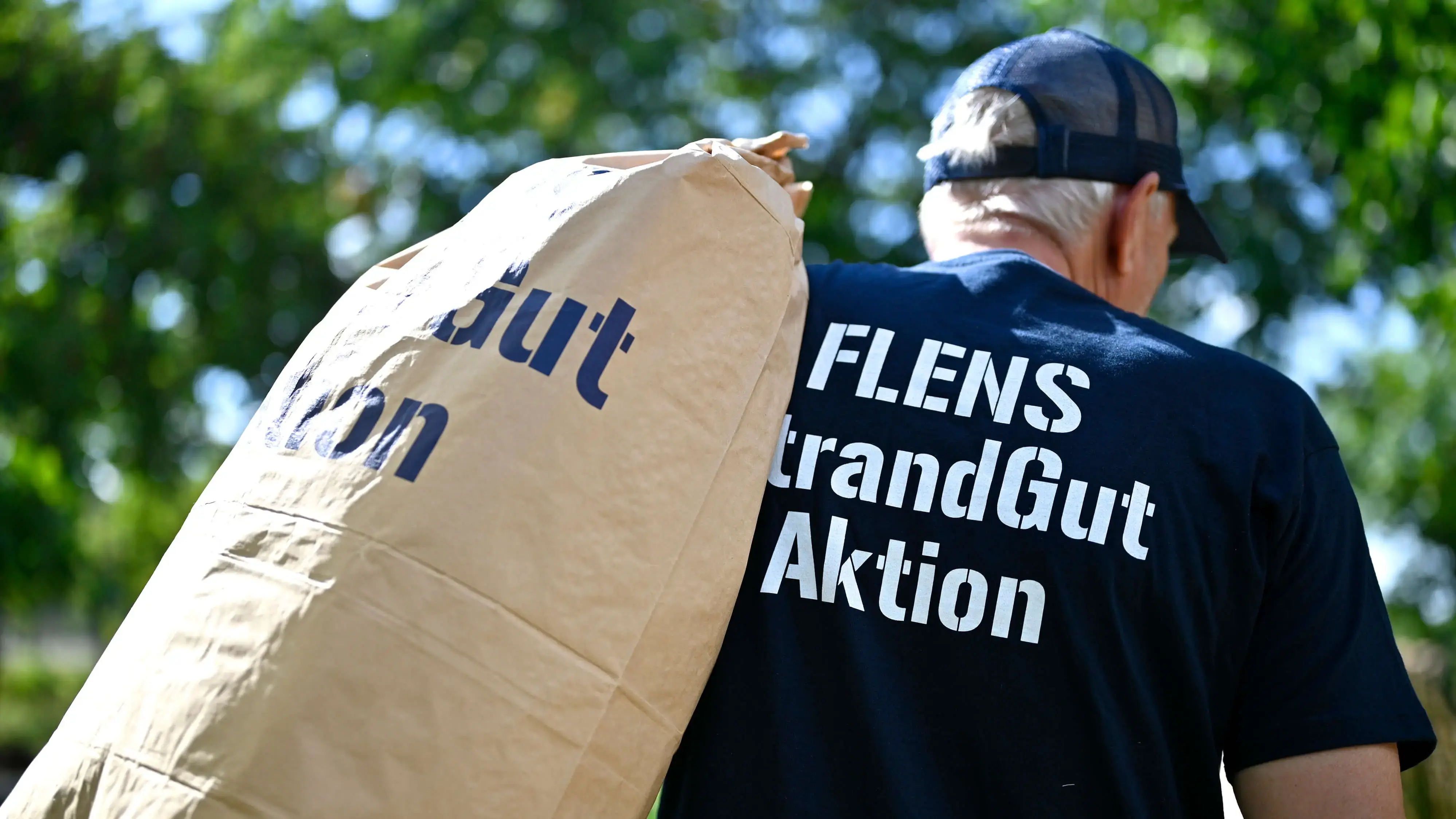 Mann trägt Sack bei Umweltschutzaktion "FLENS StrandGut" im Grünen.