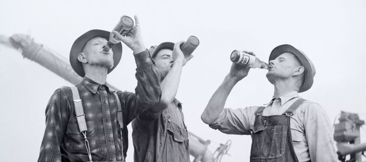 Historisches Bild dreier Männer, die aus Flensburger Bierflaschen trinken.