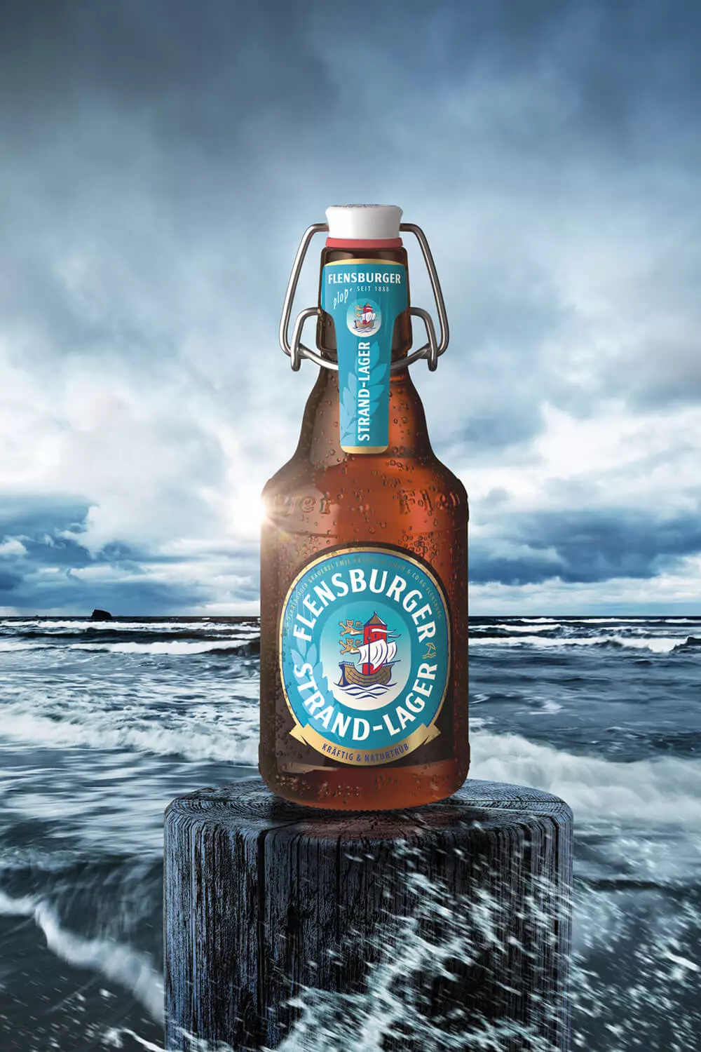 Flasche vom Flensburger Strand-Lager auf einem Poller vor einer stürmischen Strandlandschaft.