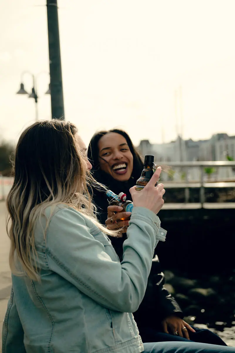 Zwei Personen am Hafen mit Flensburger-Bierflaschen – entspanntes Outdoor-Treffen bei Tageslicht.