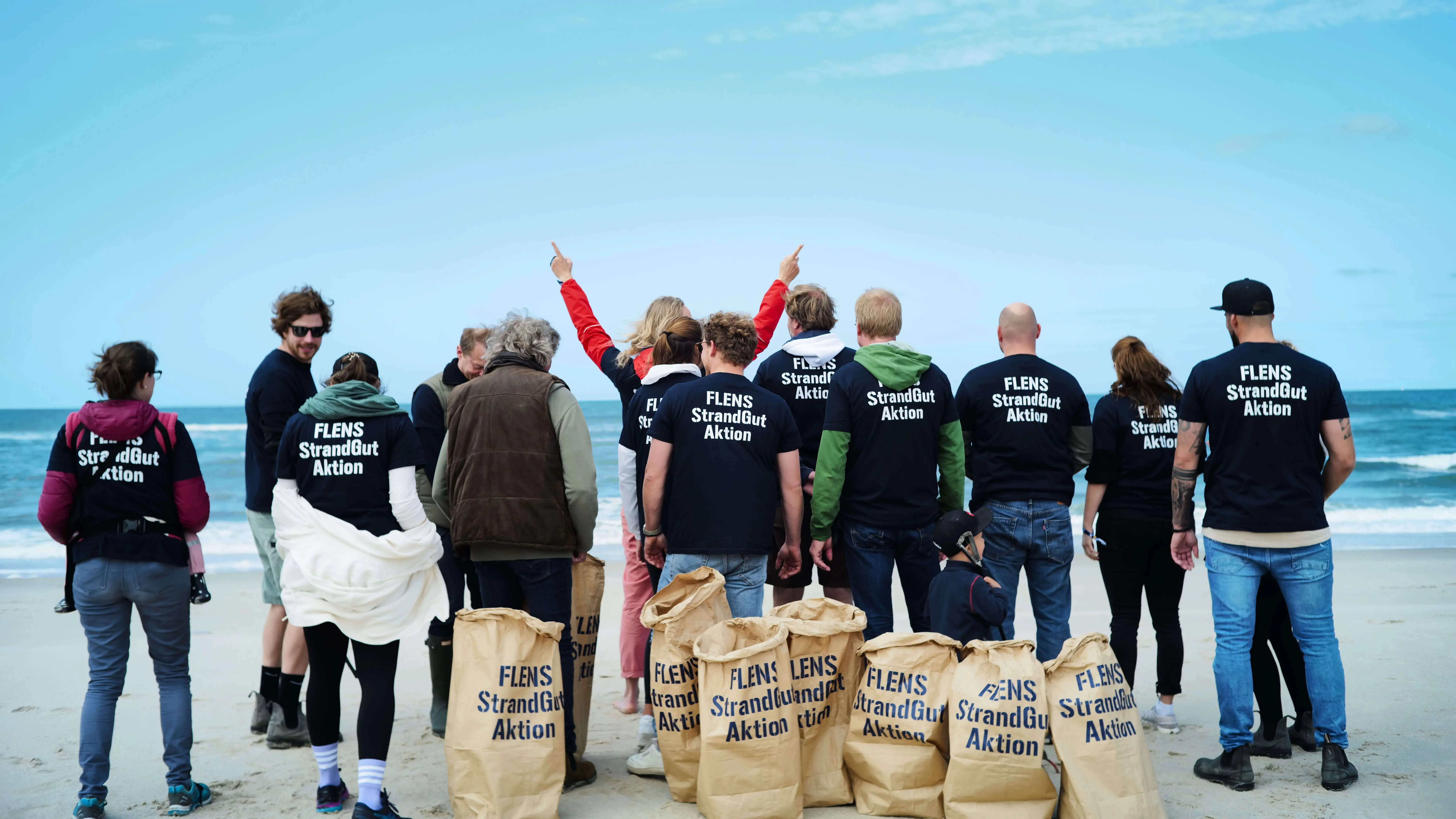 Gruppe von Freiwilligen bei einer FLENS Strandreinigungsaktion mit Säcken am Meer.