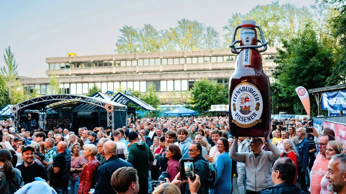 Publikum beim FLENS Festival 2025 mit einer großen, aufblasbaren FLENS Flasche.