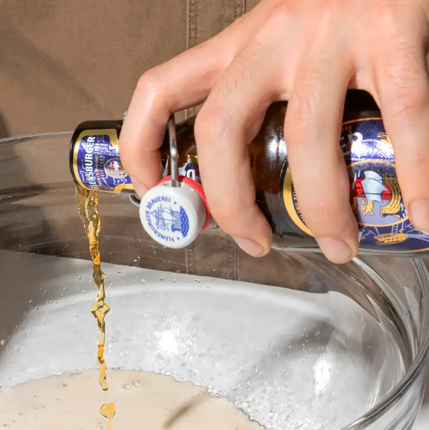 Hände gießen Flensburger Dunkel aus Bügelflasche in eine große Glasschüssel mit Mehl.