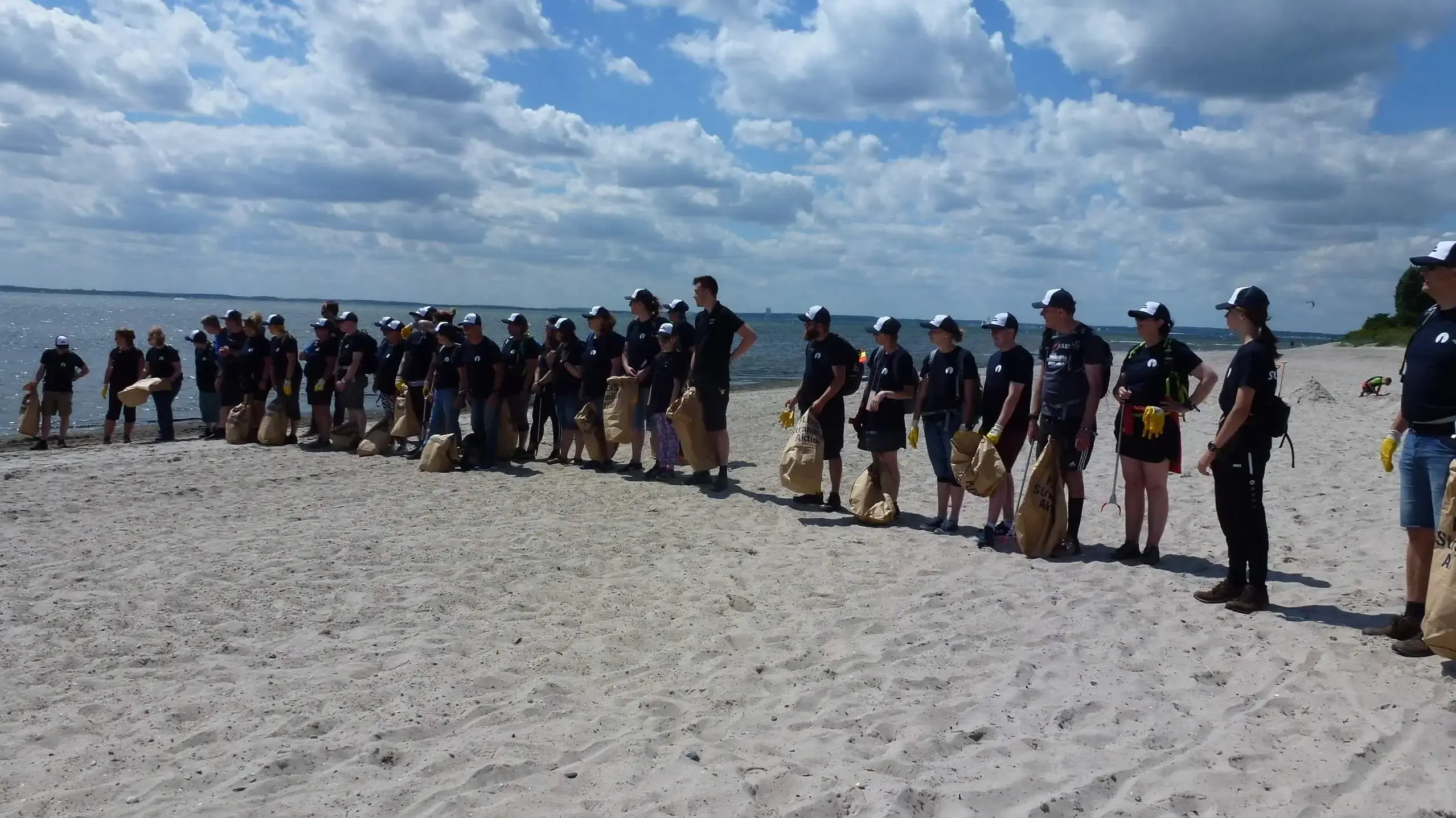 Gruppe von Freiwilligen bei einer FLENS Strandreinigung mit Säcken am Strand.