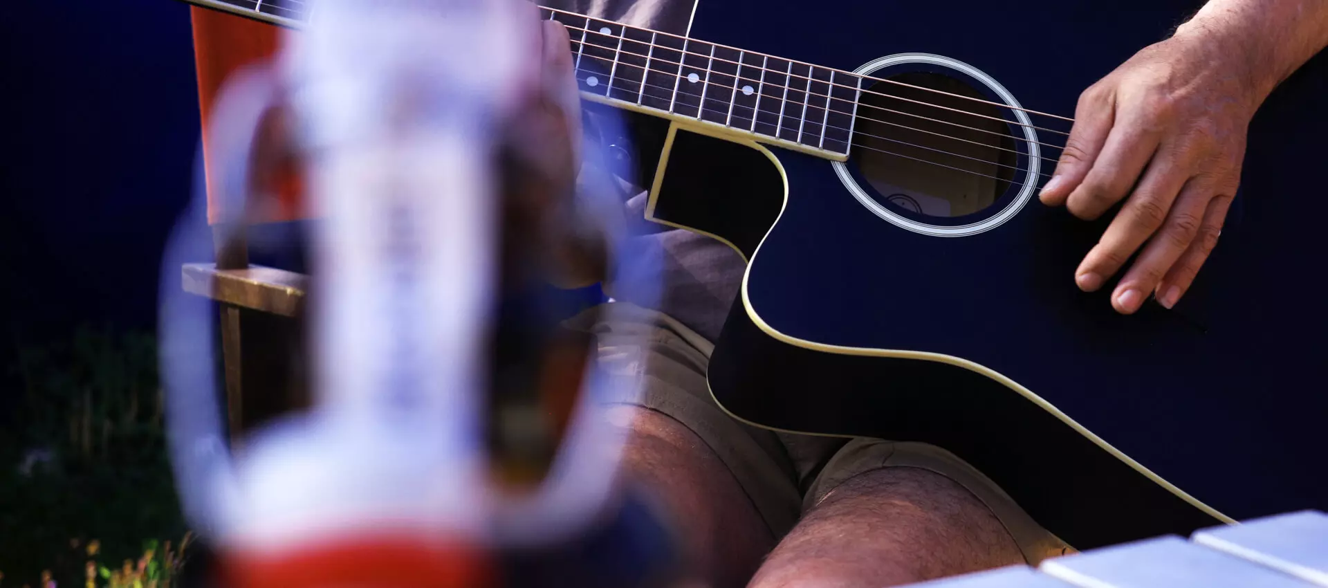 Flasche Flensburger Pilsener vorne in der Unschärfe; im Hintergrund eine Hand, die Gitarre spielt.