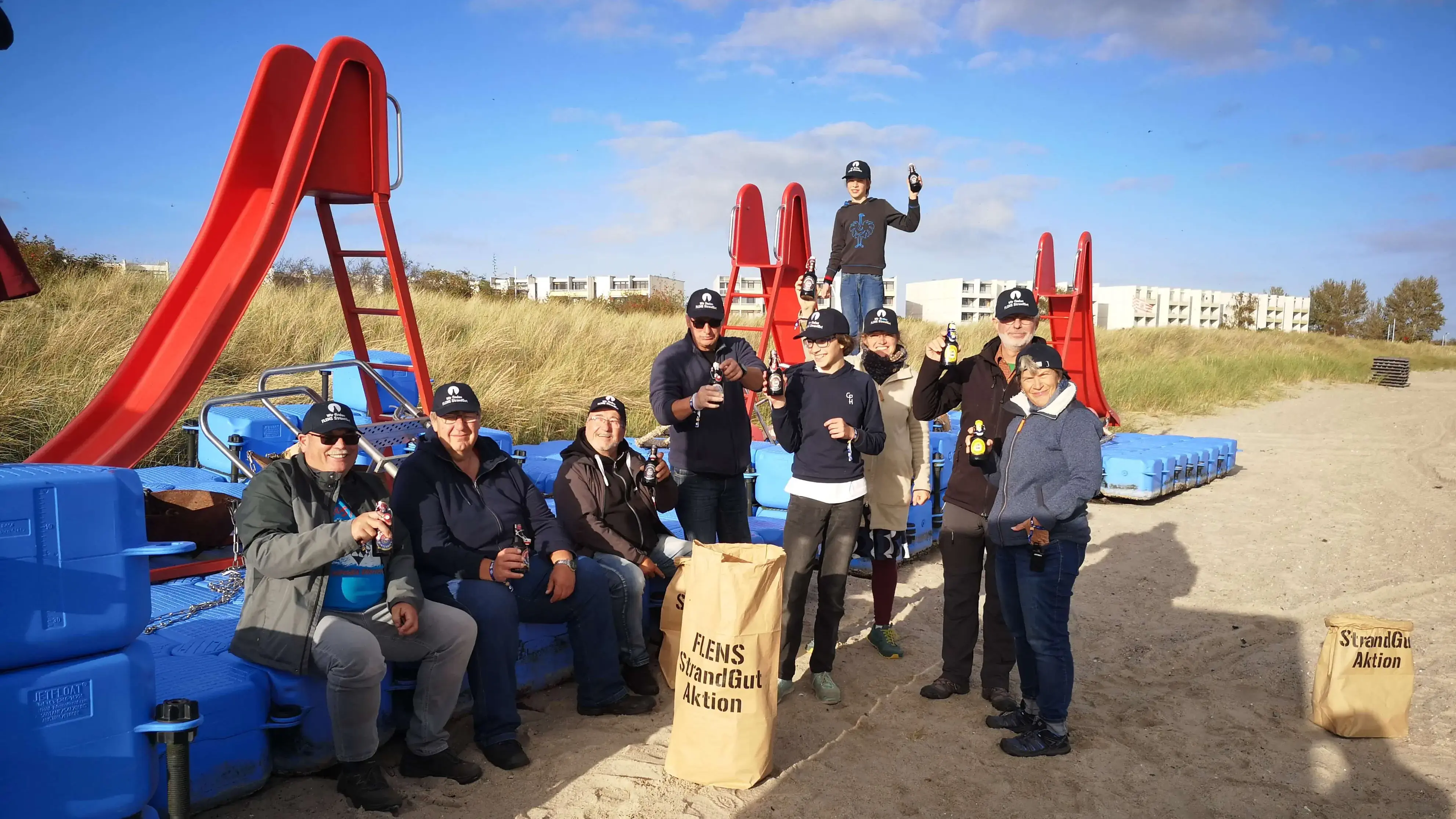Gruppe von Menschen genießt eine Pause bei der FLENS StrandGut Aktion mit FLENS Getränken und Rutsche im Hintergrund.