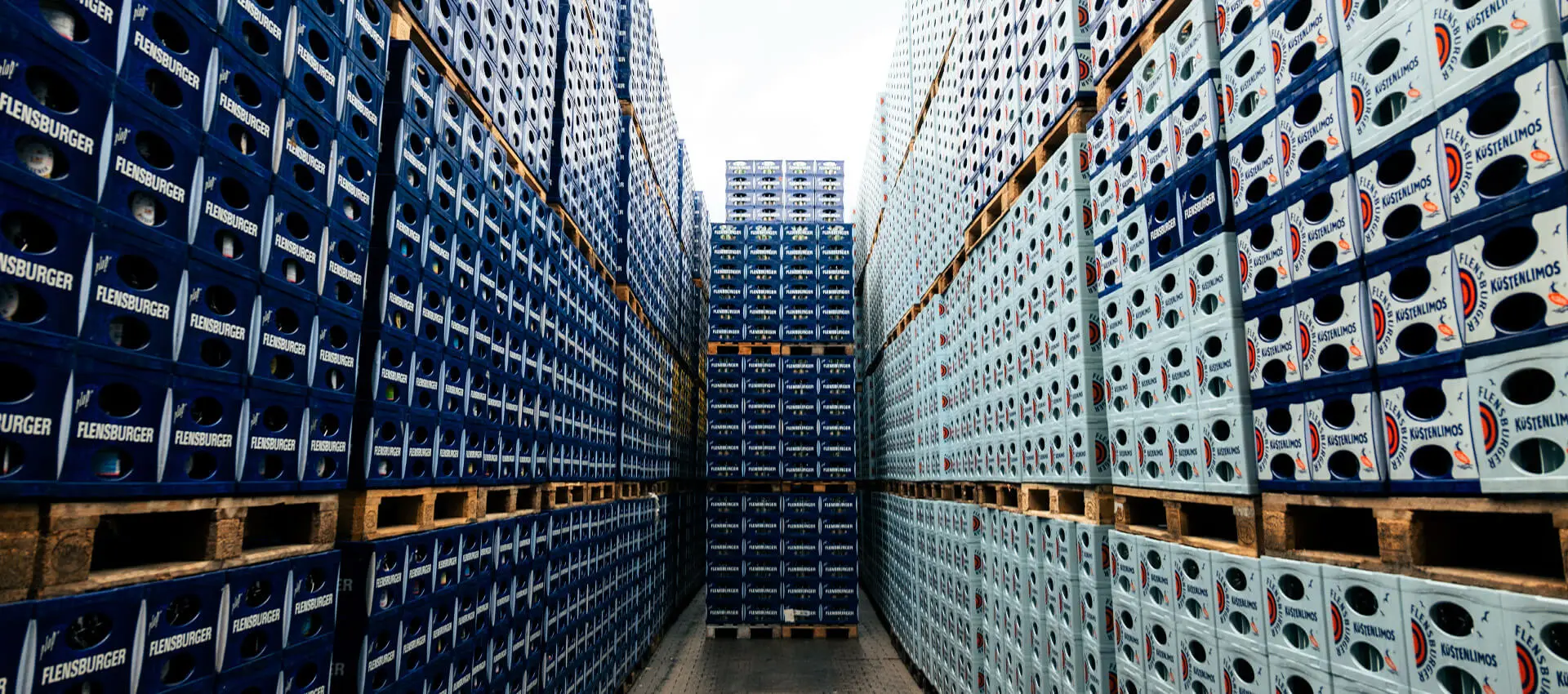 Hochgestapelte blaue Getränkekisten auf Paletten im Außenlager bei FLENS, zentrierte Optik.