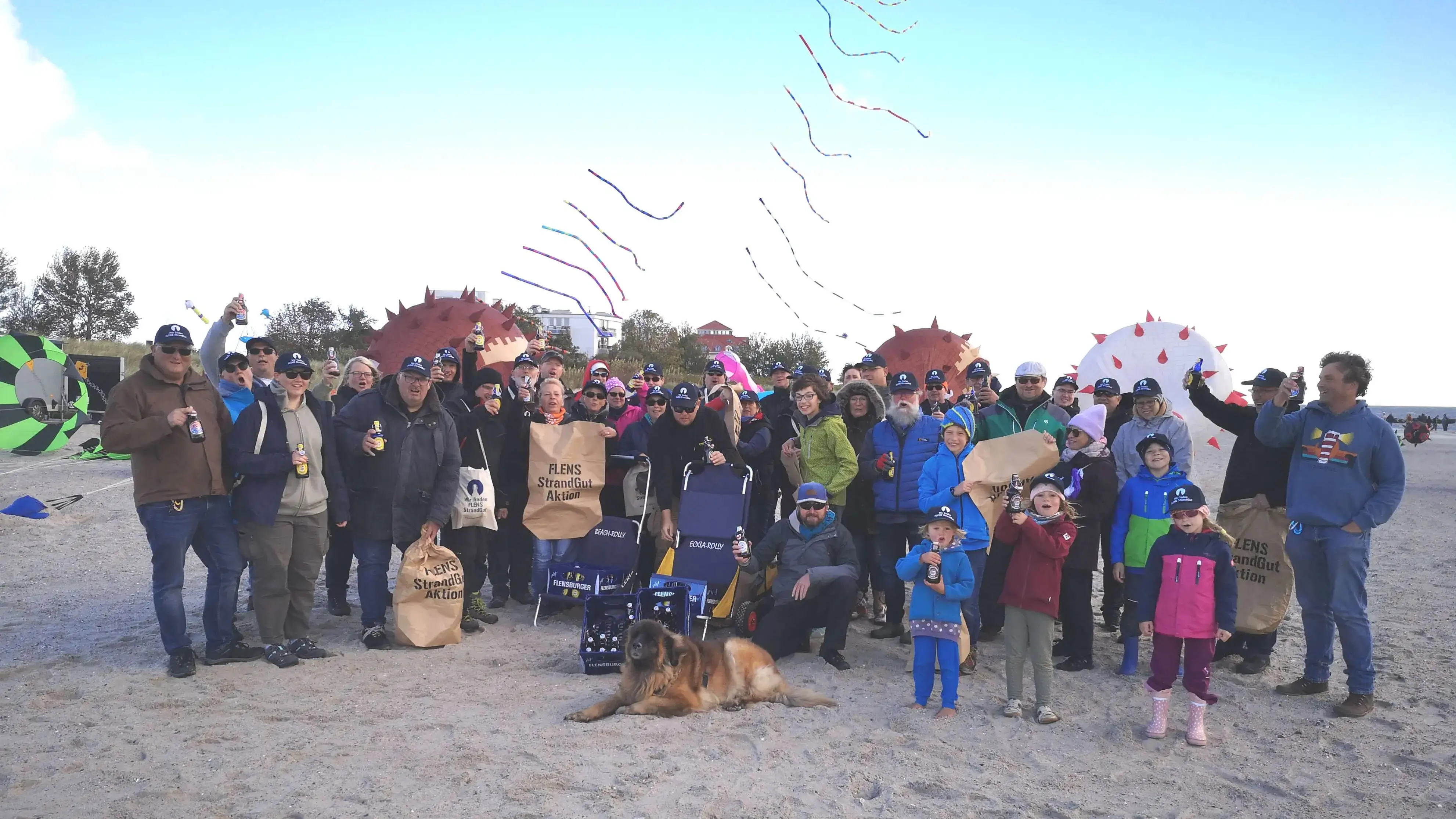 Gruppe von Personen mit Drachen am Strand bei einem FLENS StrandGut Event.