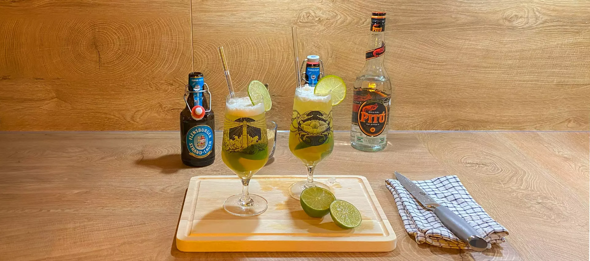 In einer Holzküche stehen zwei appetitlich aussehende Gläser mit dem Biercocktail Caibierinha vor den Cocktail-Utensilien.