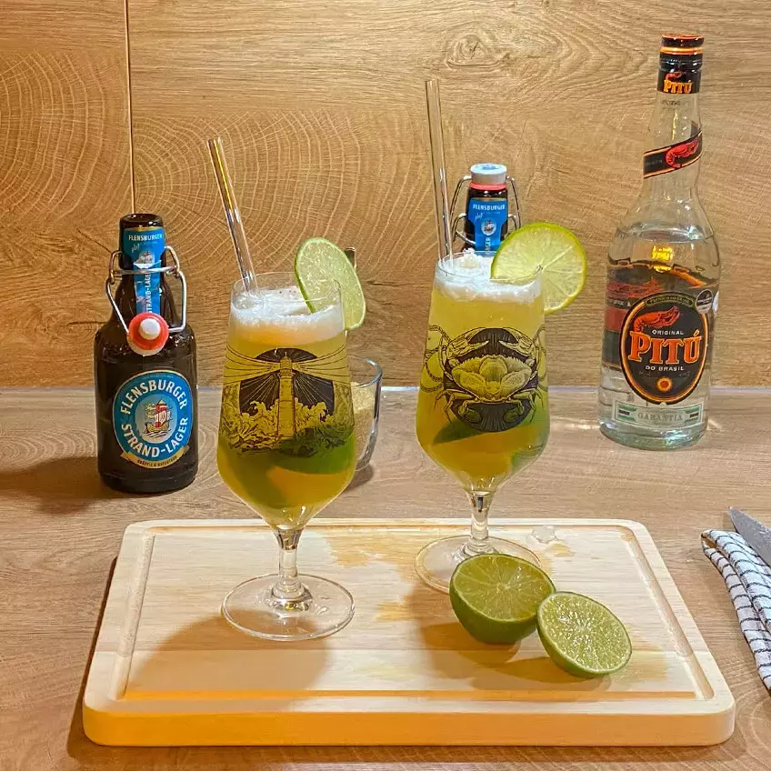 In einer Holzküche stehen zwei appetitlich aussehende Gläser mit dem Biercocktail Caibierinha vor den Cocktail-Utensilien.