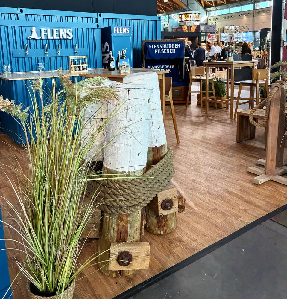 Flensburger Pilsener Bierstand auf Messe: blaues Container-Design, Bar-Tische, Holz- und maritime Schiffstau-Deko.