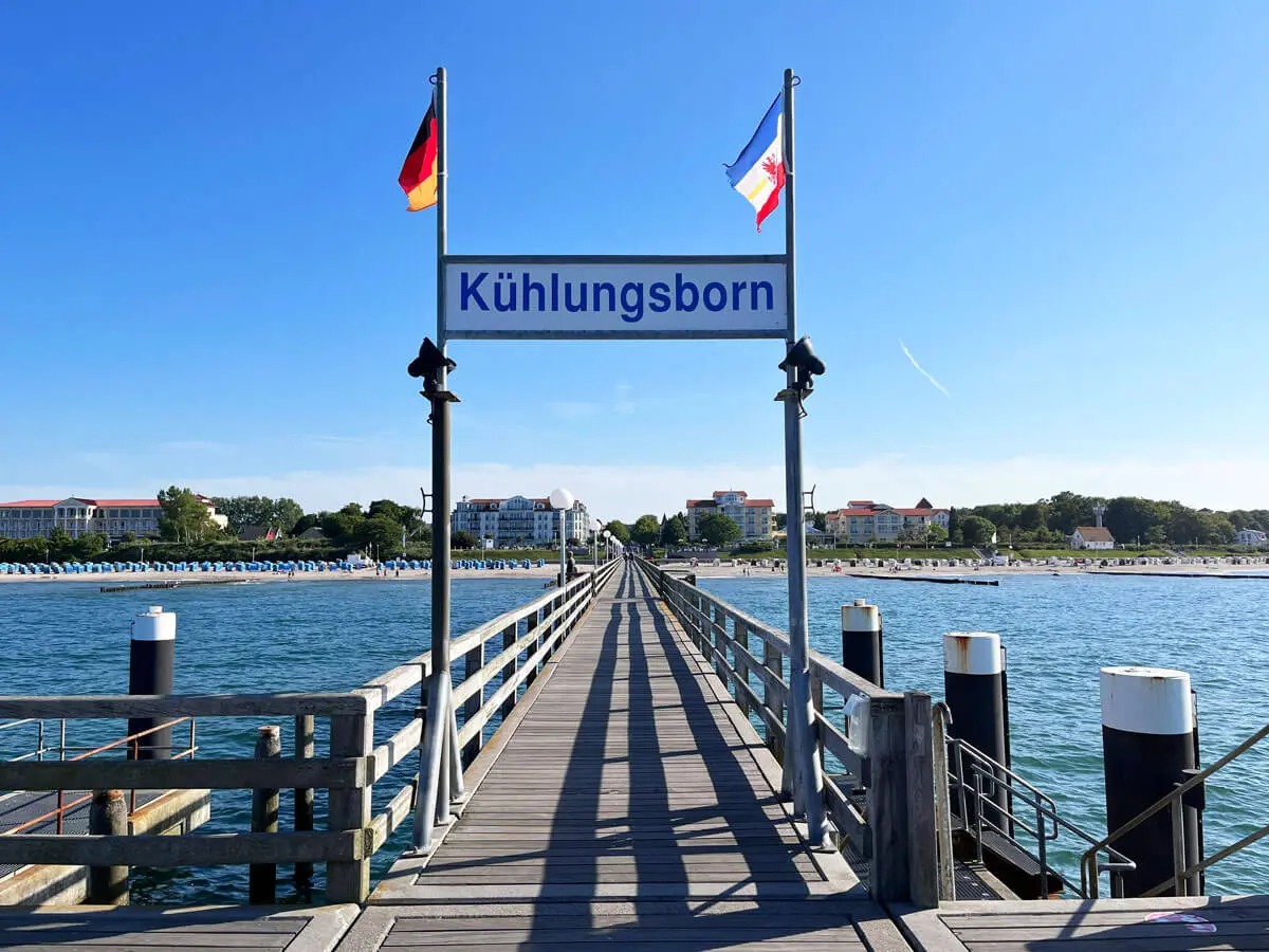 Seebrücke in Kühlungsborn: Holzsteg mit Ortsschild, deutschen Flaggen und Ostsee-Blick zum Strand.