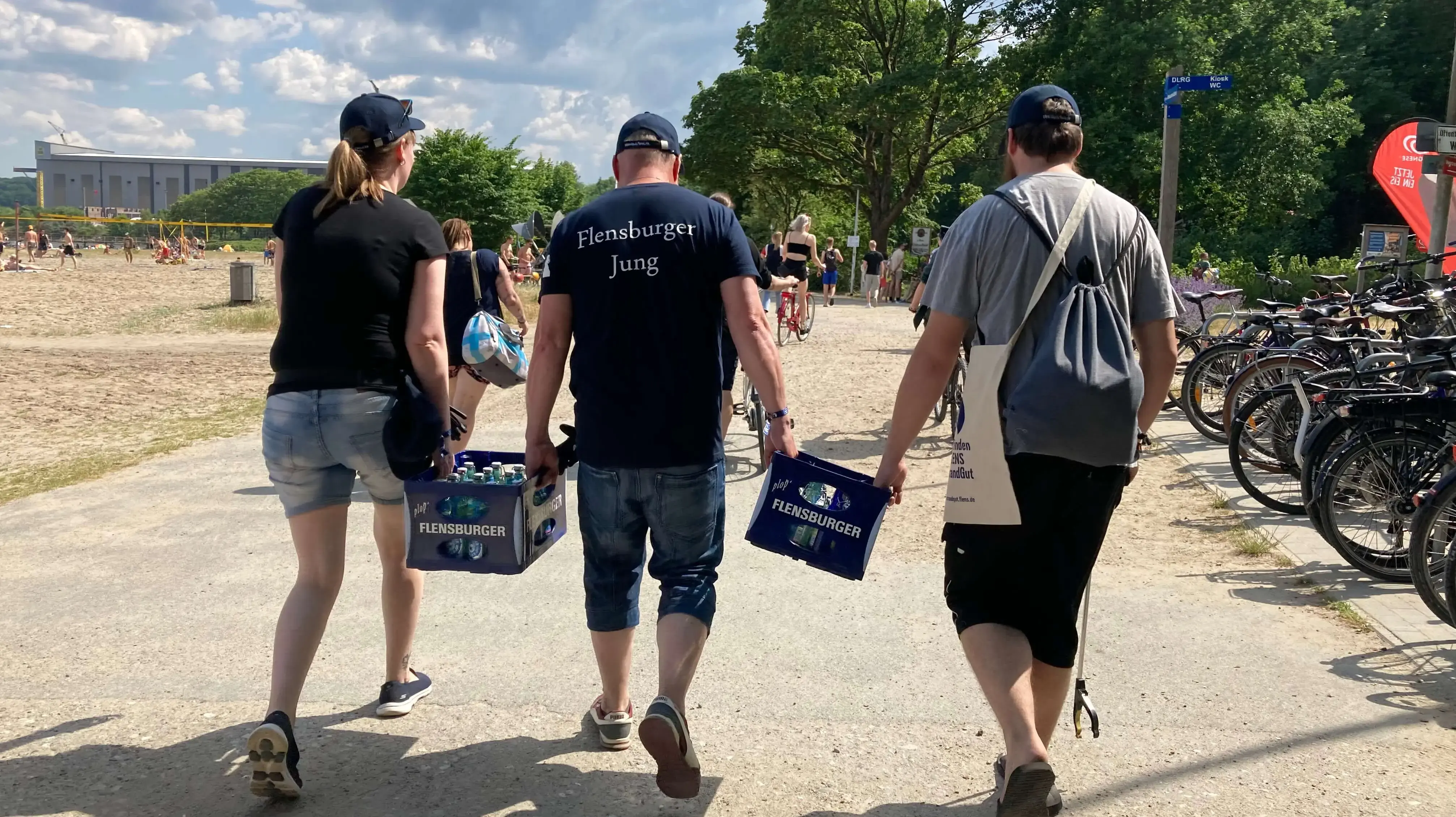 Drei Personen gehen mit Flensburger Kästen am Strand zu einer FLENS Strandreinigungsaktion.