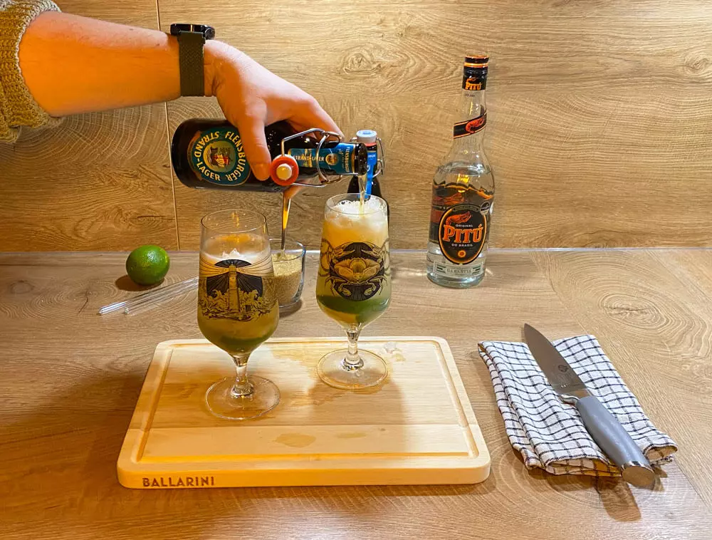 Flensburger Strand-Lager wird ins Cocktailglas eingeschenkt, dahinter Cocktailutensilien.