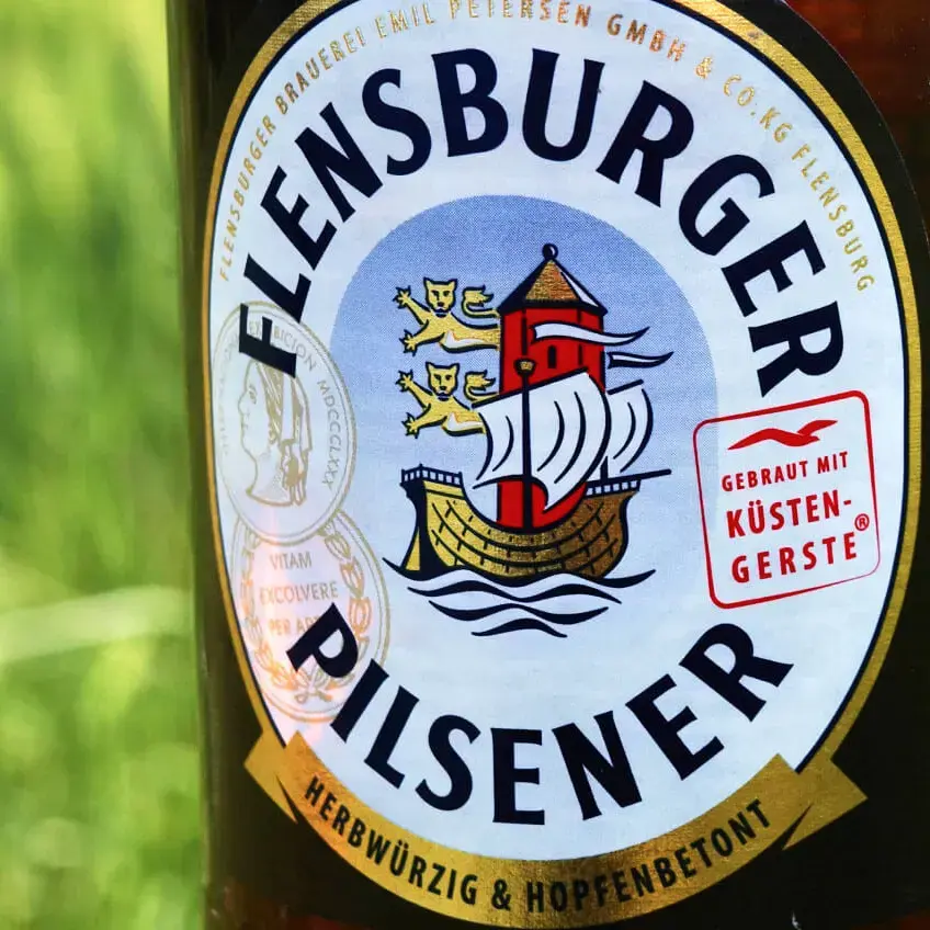 Etikett vom Flensburger Pilsener im Anschnitt vor einer grünen Wiese.