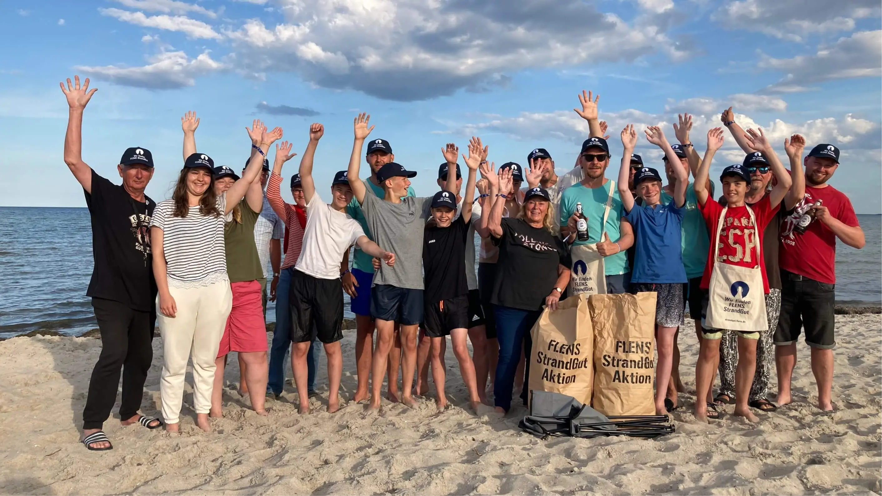 Gruppe von Menschen jubelt am Strand bei einer FLENS Strandreinigungsaktion.