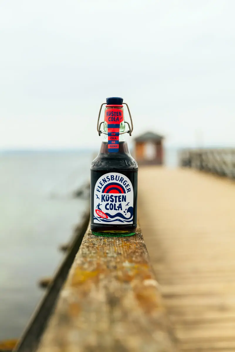 Flensburger Küstencola-Glasflasche auf Holzpier am Meer, maritime Erfrischung an der Ostsee.