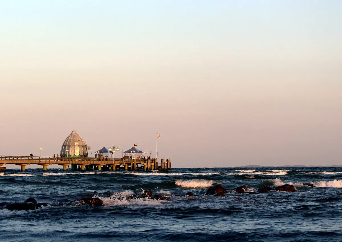 Seebrücke von Grömitz mit Tauchglocke, Spaziergängern und Brandung im Meer bei pastellfarbenem Sonnenuntergang.