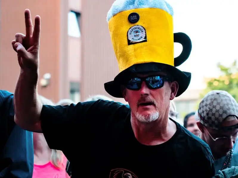 Mann mit Bier-Hut zeigt das Piece-Zeichen beim FLENS Festival 2025.