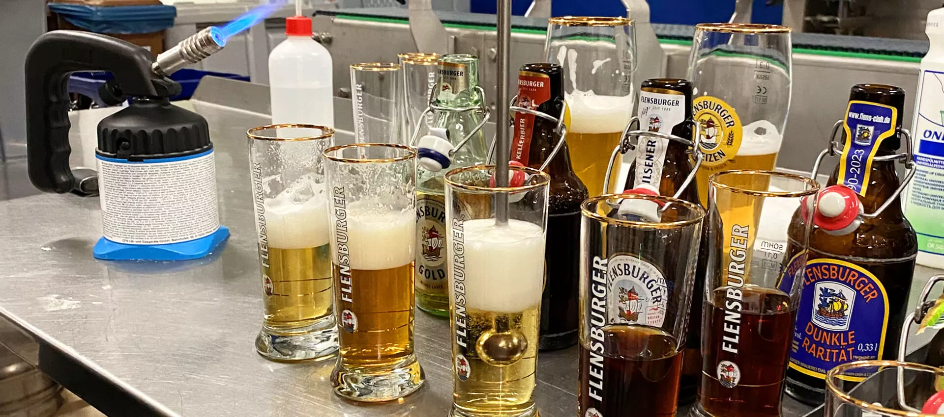 Mehrere Biersorten in FLENS Gläser eingeschenkt, dahinter die dazugehörigen Flaschen, der Bierstachel im mittleren Glas.