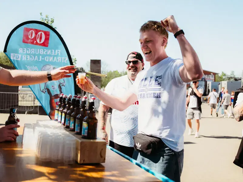 Mann jubelt am Flensburger-Stand bei Sommerwetter beim Prömpelspiel.