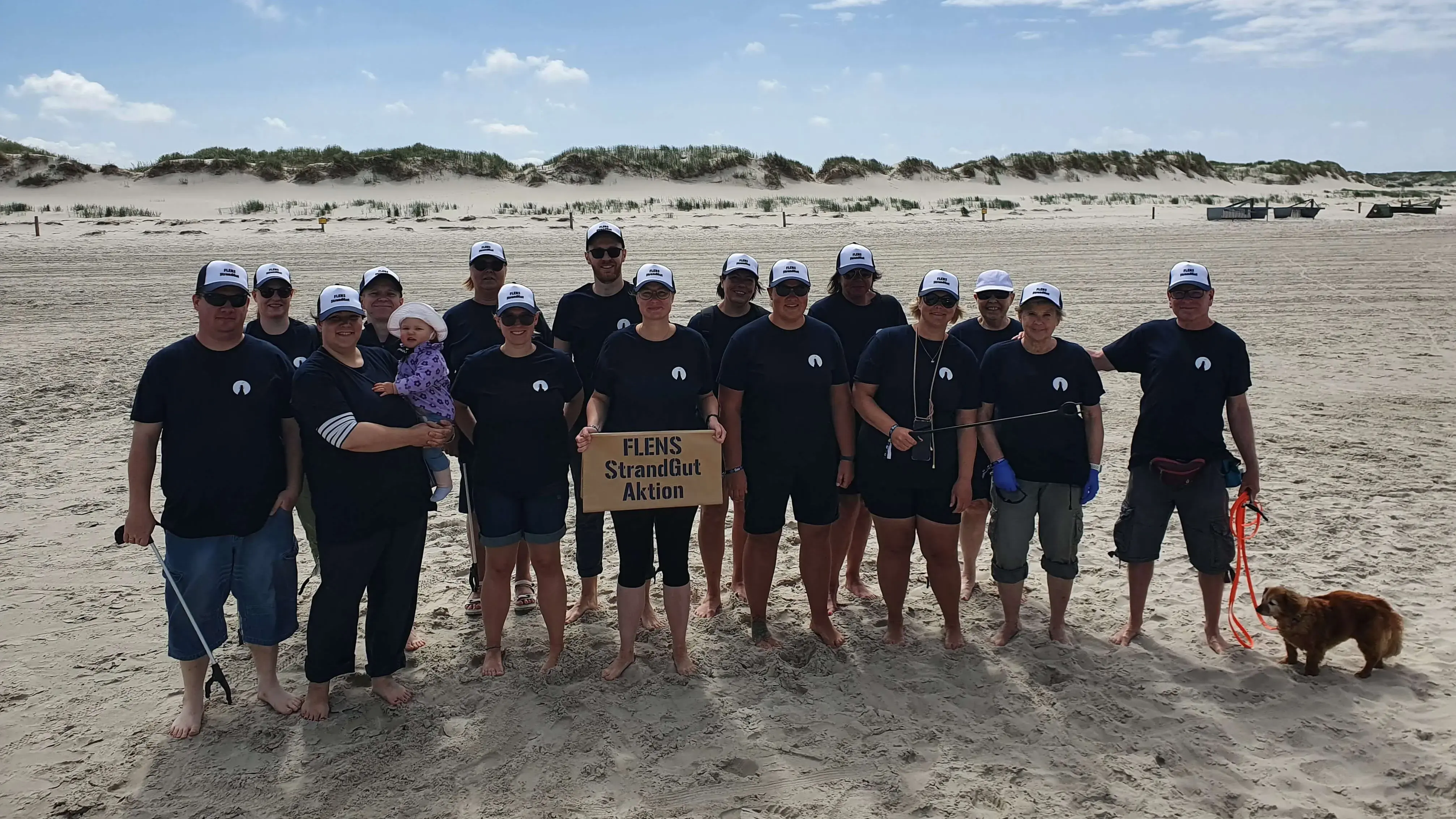 Gruppe von Menschen in einheitlichen FLENS StrandGut T-Shirts bei Strandreinigungsaktion.