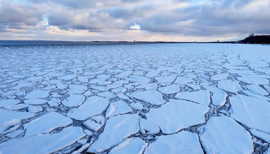 Zerklüftete Eisschollen auf gefrorenem Meer vor Küste unter blauem Winterhimmel.