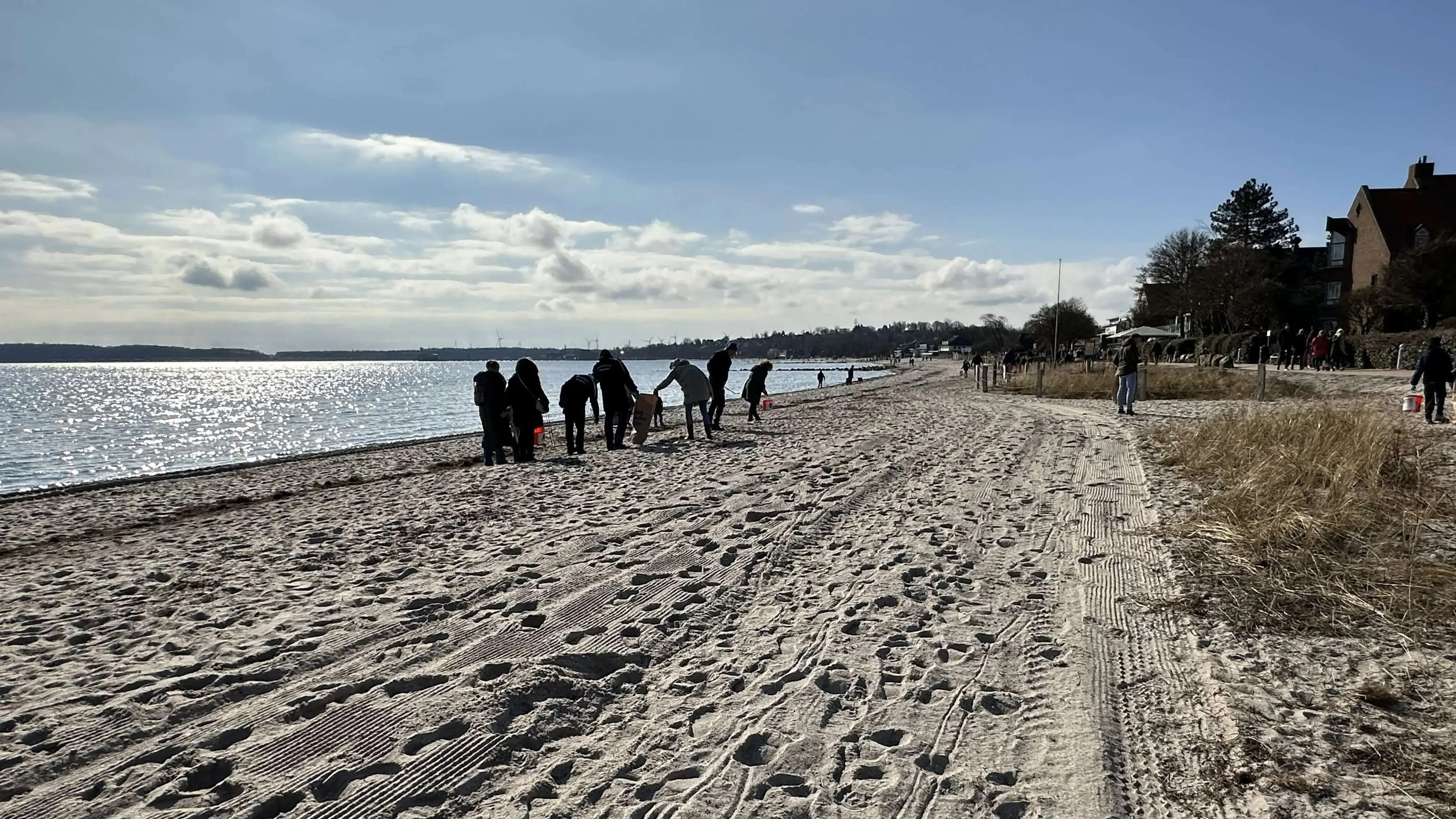 Freiwillige bei einer FLENS StrandGut Aktion neben glitzerndem Wasser.
