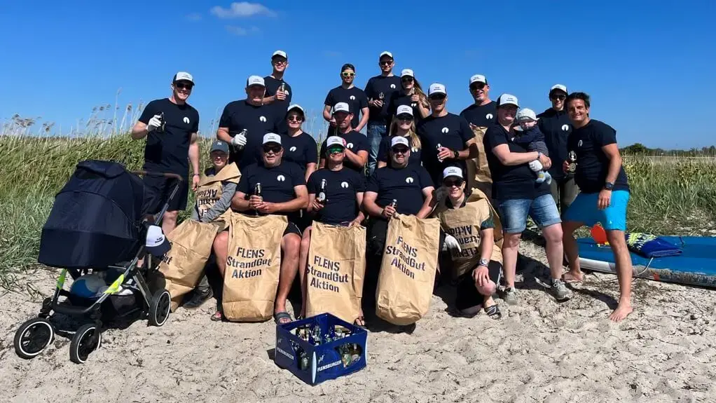 Gruppe von Freiwilligen bei einer FLENS Strandreinigungsaktion auf hellem Sand.