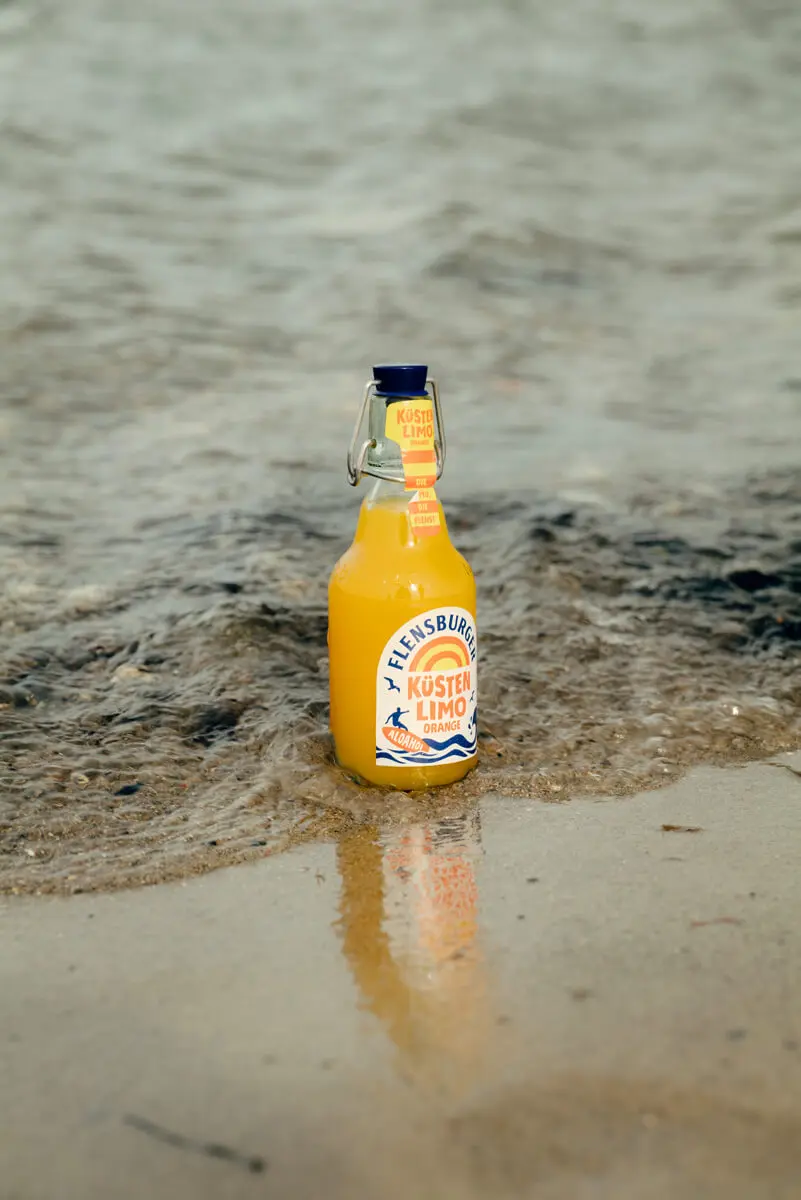 Küstenlimo Orange im seichten Meerwasser in der Welle am Sandstrand mit Reflexion.